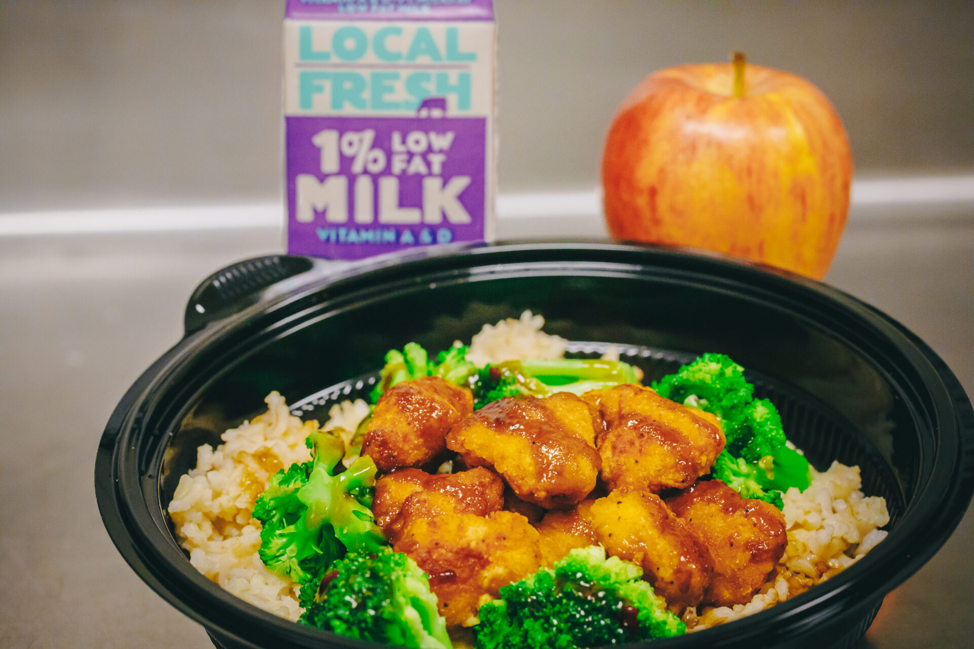 Image of a school lunch with milk, an apple, and broccoli chicken on brown rice.
