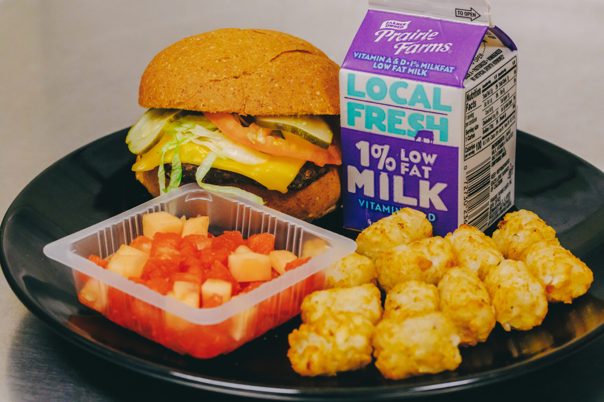 Image of a school lunch with a cheeseburger, milk, tater tots and bell peppers.