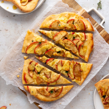 Baked Brie and Apple Flatbread on a cutting board with a few pieces plated.
