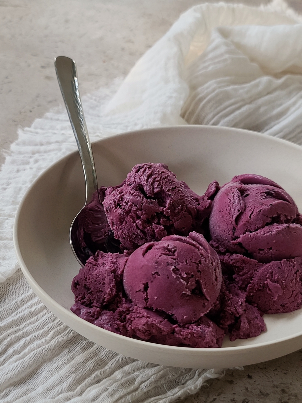 Bowl of blueberry pie ice cream on a countertop with tea towel below.