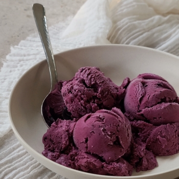 Bowl of blueberry pie ice cream on a countertop with tea towel below.