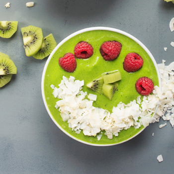 Green Smoothie Bowl with Coconut, kiwi, and raspberries on a gray surface.