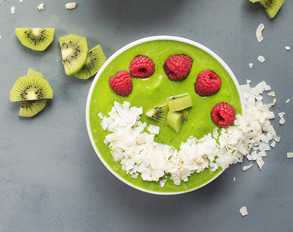 Green Smoothie Bowl with Coconut, kiwi, and raspberries on a gray surface.