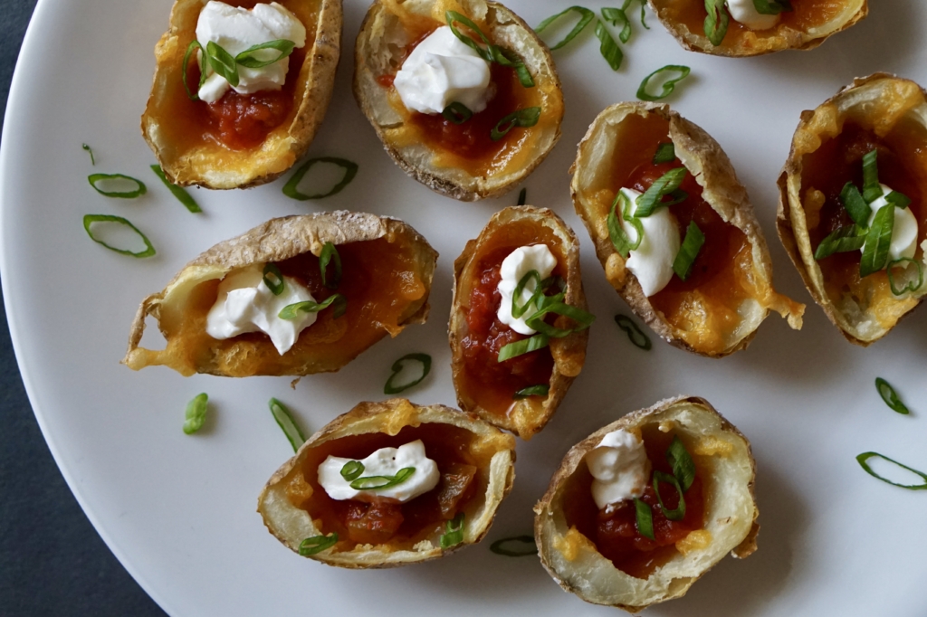 Mini potato skins on white plate topped with sour cream and green onions.