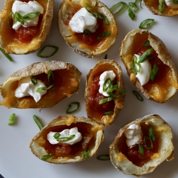 Mini potato skins on white plate topped with sour cream and green onions.