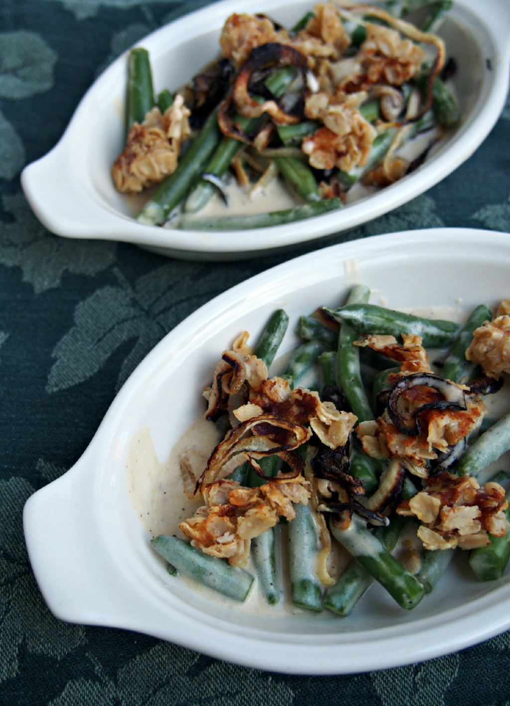 Two dishes of modern green bean casserole on a table cloth.