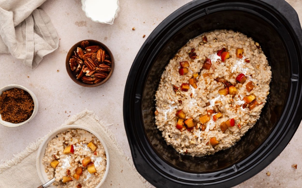 Slow cooker with apple cinnamon steel cut oats with pecans, brown sugar, and peaches.