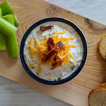 Bacon and cheddar dip on a serving board with celery sticks and bread slices
