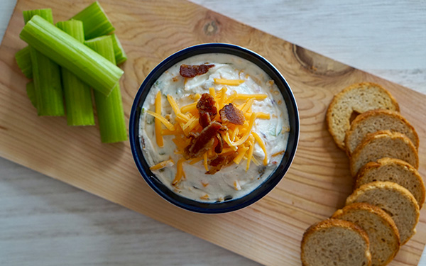 Bacon and cheddar dip on a serving board with celery sticks and bread slices