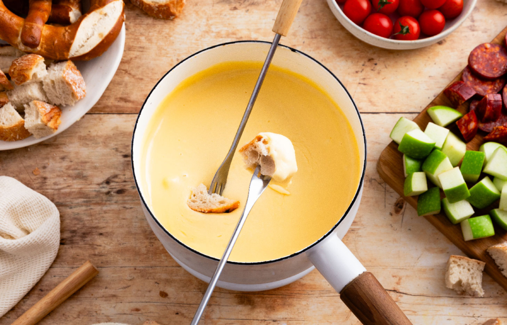 Image of skewers dipping bread pieces into creamy beer cheese fondue.