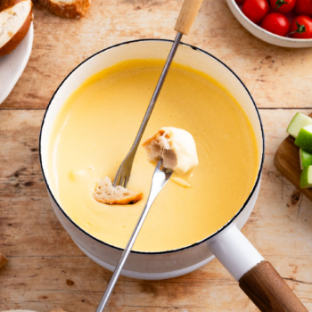 Image of skewers dipping bread pieces into creamy beer cheese fondue.