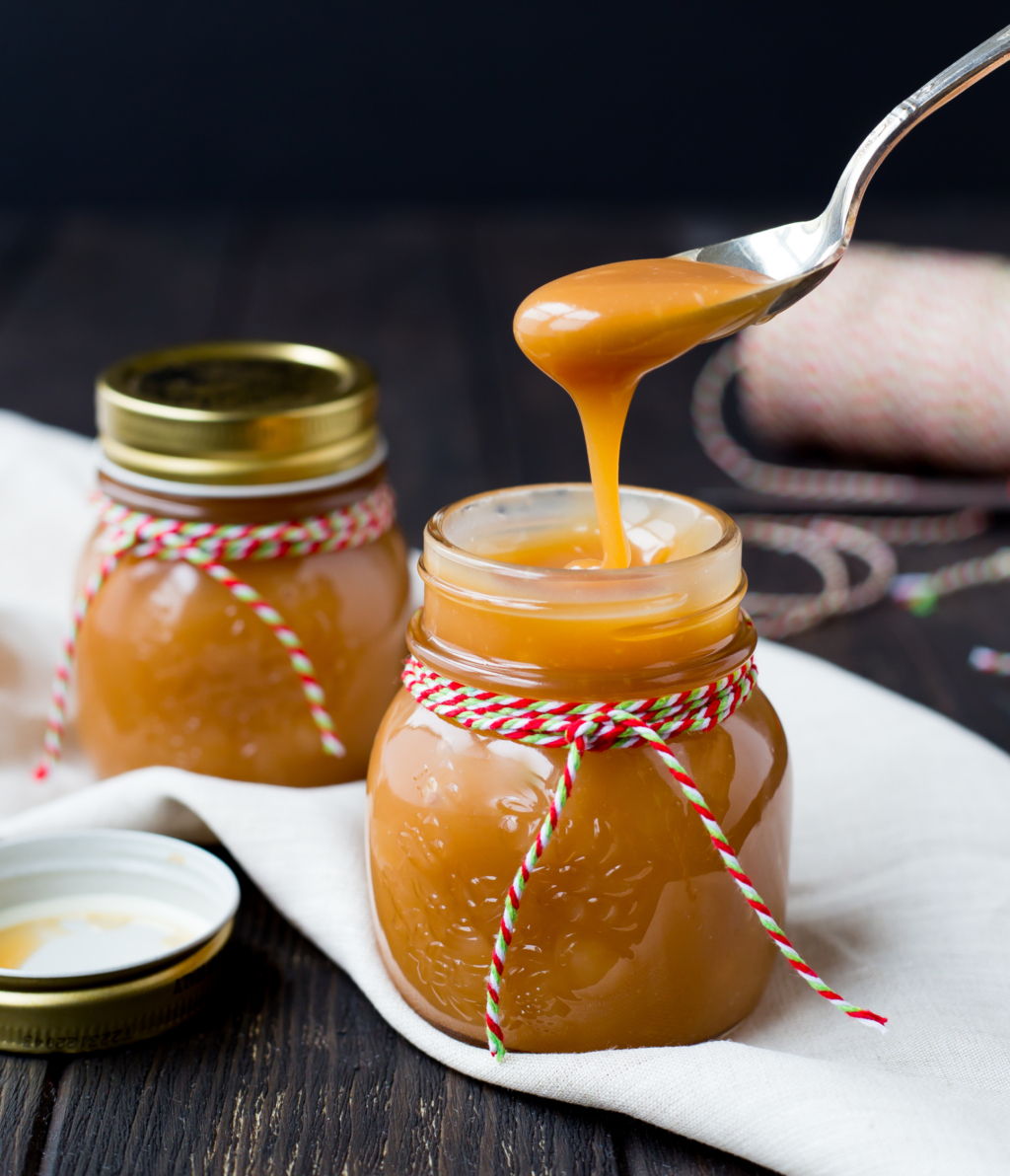 Spoon dishing out of a jar of bourbon caramel sauce on a wooden table wrapped for the holidays.
