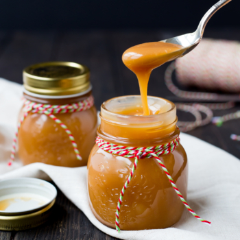 Spoon dishing out of a jar of bourbon caramel sauce on a wooden table wrapped for the holidays.