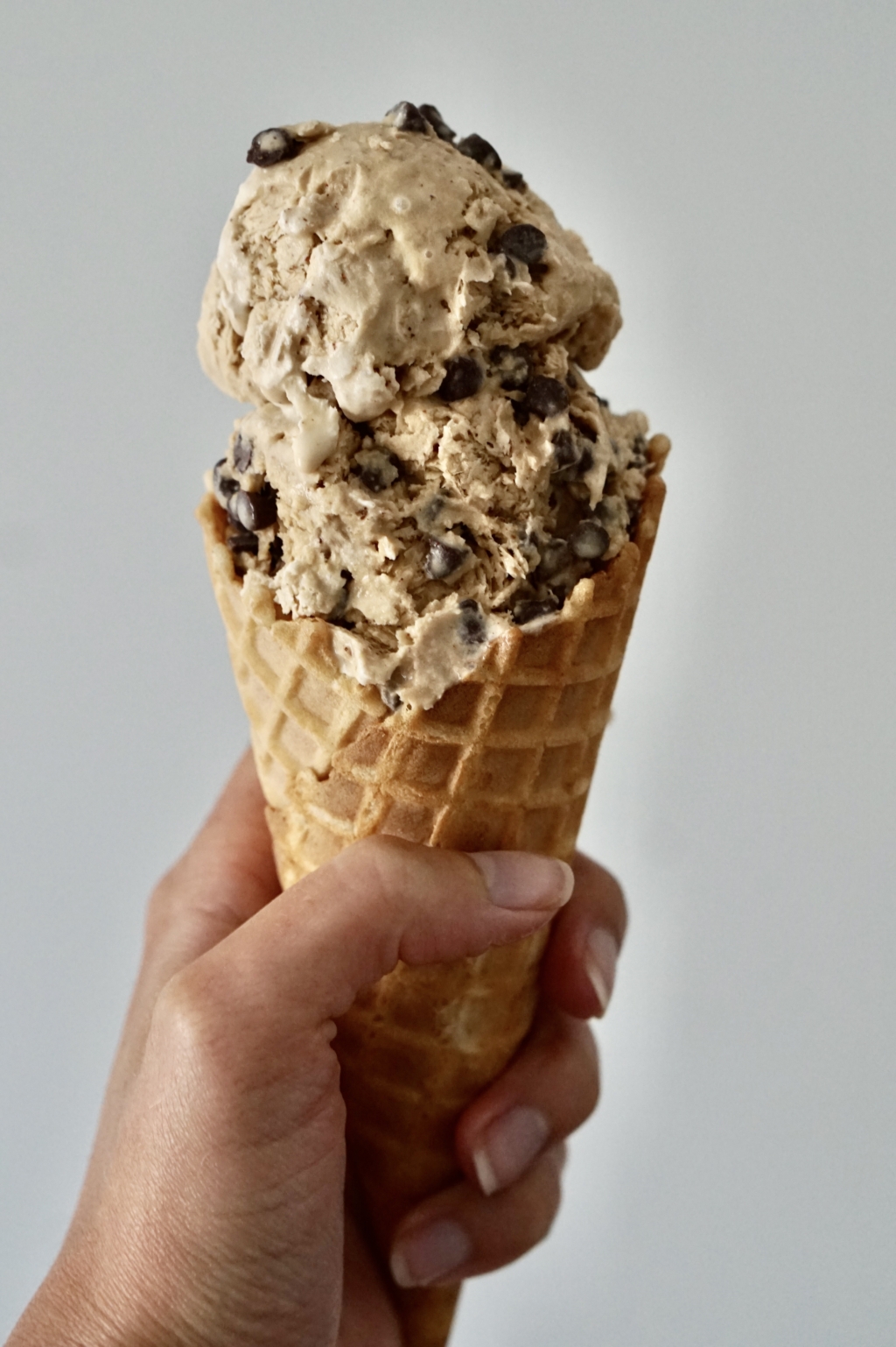 Image of a hand holding a waffle cone with two scoops of cappuccino chocolate chip ice cream