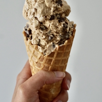 Image of a hand holding a waffle cone with two scoops of cappuccino chocolate chip ice cream