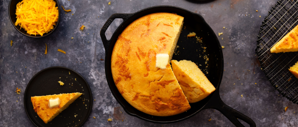 Image of freshly baked cheesy buttermilk corn bread in a cast iron skillet with a pad of butter melting on top.