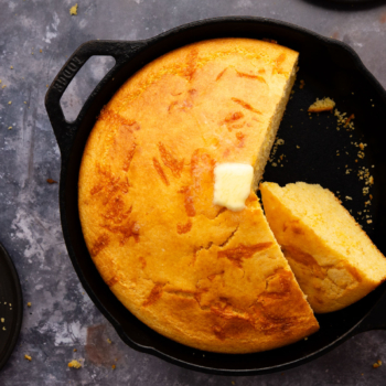 Image of freshly baked cheesy buttermilk corn bread in a cast iron skillet with a pad of butter melting on top.