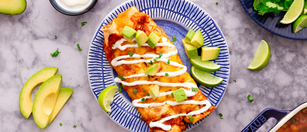 Overhead image of cheesy turkey enchiladas on a plate drizzled with sour cream.