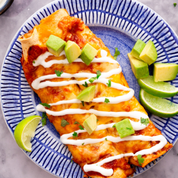 Overhead image of cheesy turkey enchiladas on a plate drizzled with sour cream.