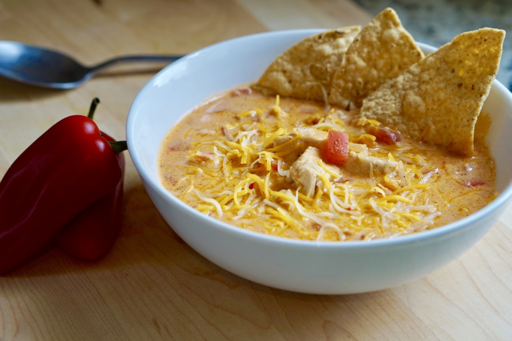 Image of a bowl filled with chicken taco soup topped with shredded cheese and tortilla chips.
