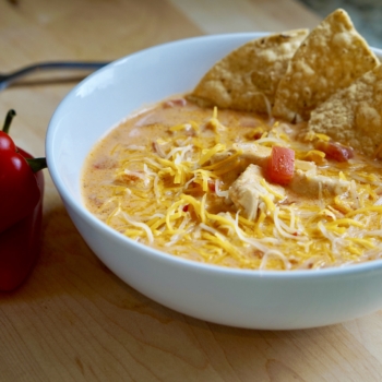 Image of a bowl filled with chicken taco soup topped with shredded cheese and tortilla chips.