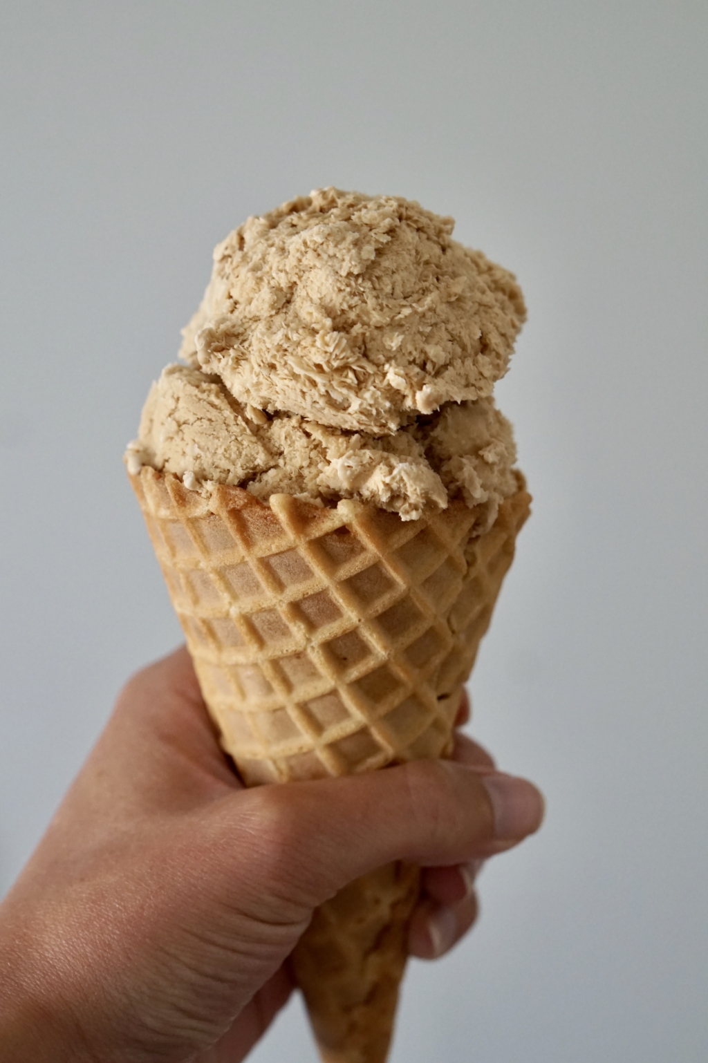 Image of a hand holding a waffle cone with a scoop of coffee ice cream.