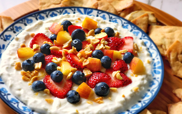 Image of creamy fruit-topped dip in a bowl surrounded by pita chips.