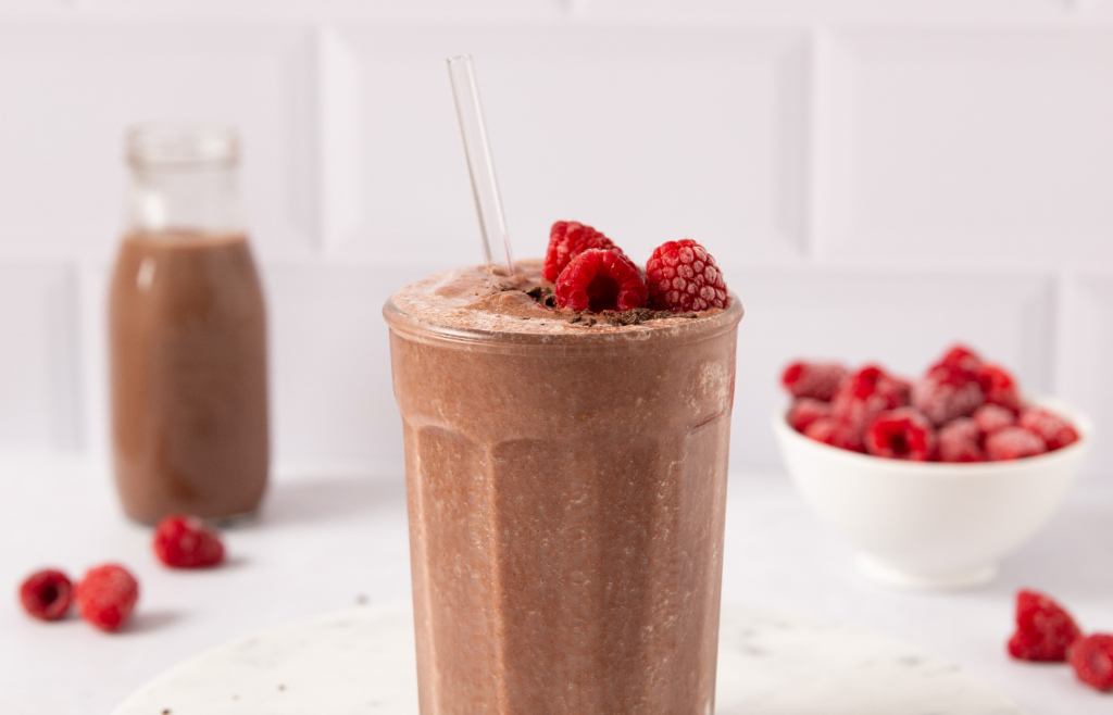 Image of dark chocolate raspberry smoothie in a glass topped with raspberries and chocolate shavings.