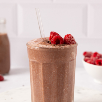 Image of dark chocolate raspberry smoothie in a glass topped with raspberries and chocolate shavings.