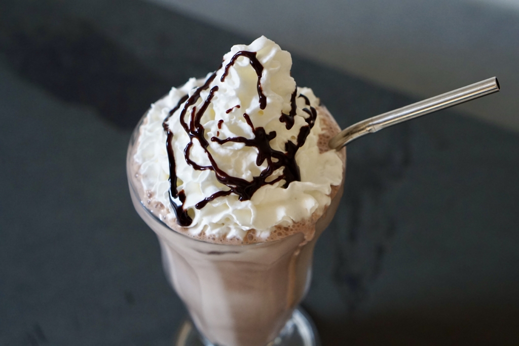 Image of chocolate milkshake with whipped cream and chocolate syrup drizzle.