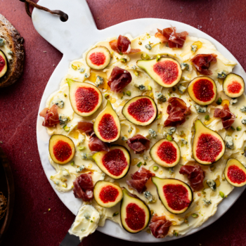 Overhead image of a butter board topped with sliced figs, prosciutto, bleu cheese and nuts.