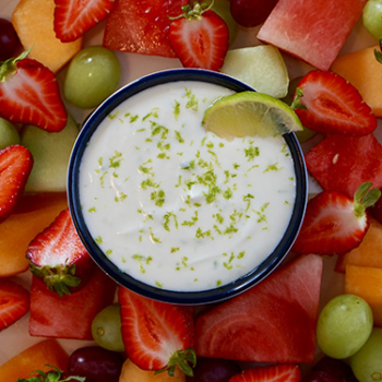 Overhead image of fresh fruit surrounding a bowl of creamy lime dip.
