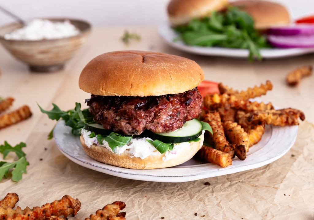 Image of a Greek Cheese Burger on a plate with crinkle fries.