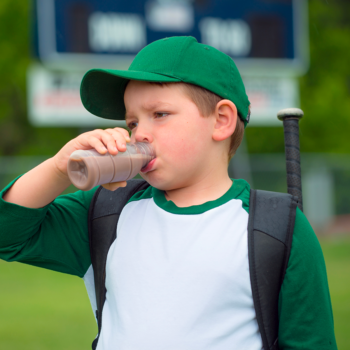 Child baseball player drinking chocolate milk after game.